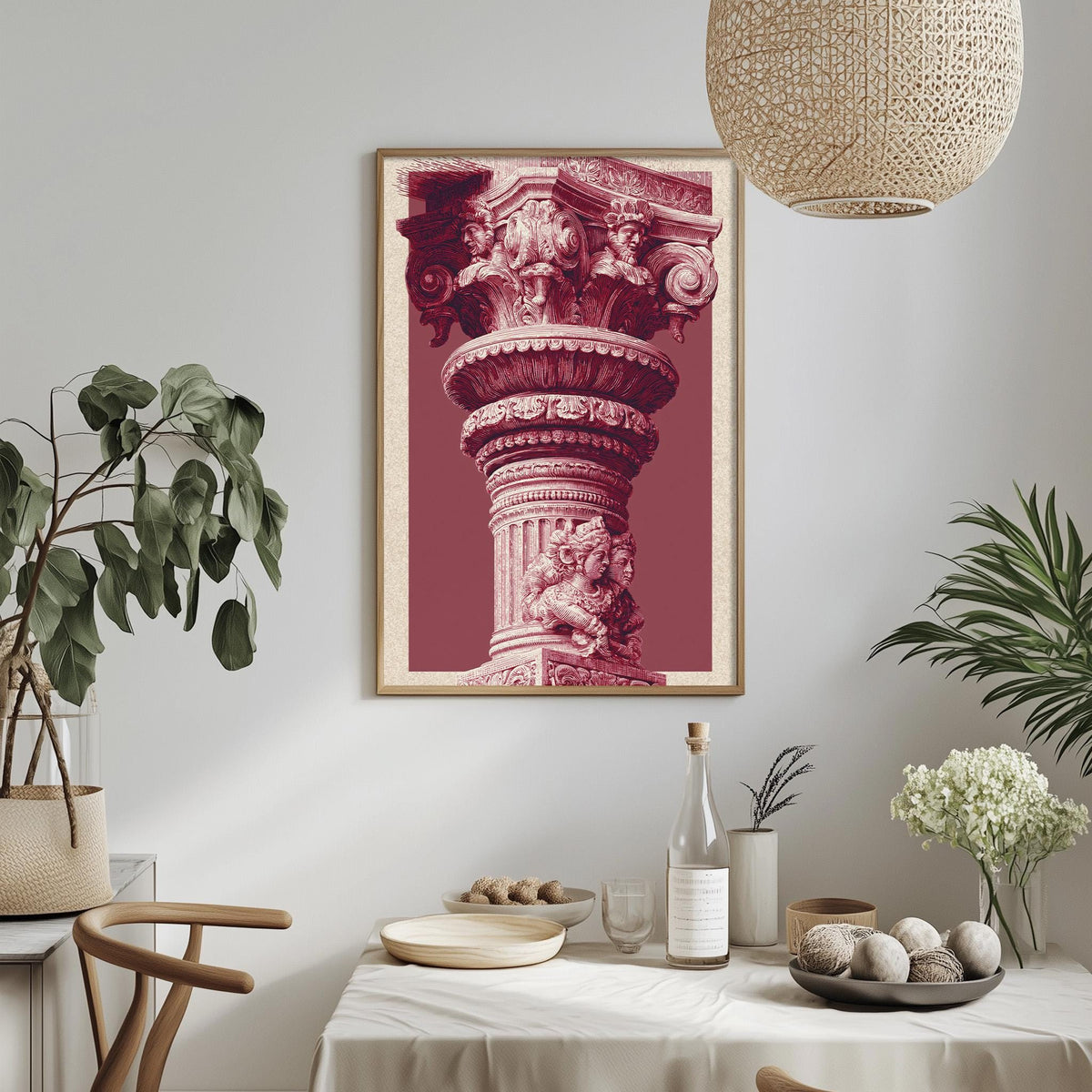 a dining table with a white tablecloth, a bowl of fruit, a bottle, and a vase with flowers. Above the table, there is a framed picture of a column with intricate carvings.