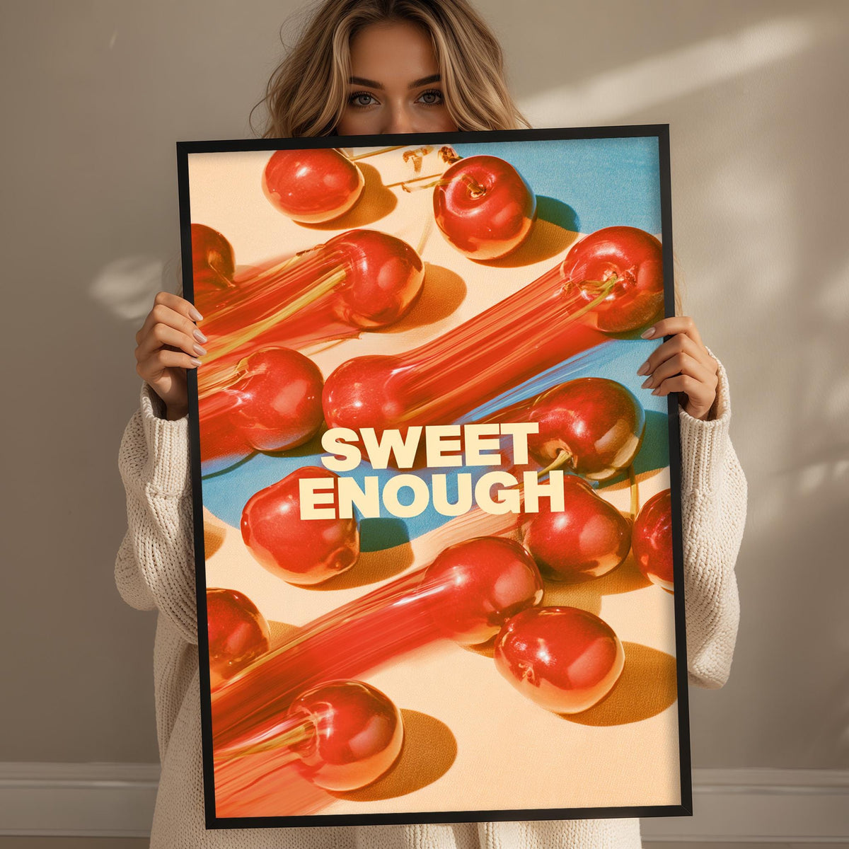 A woman holding a framed poster with a vibrant image of red apples and the text "Sweet Enough" written on it.