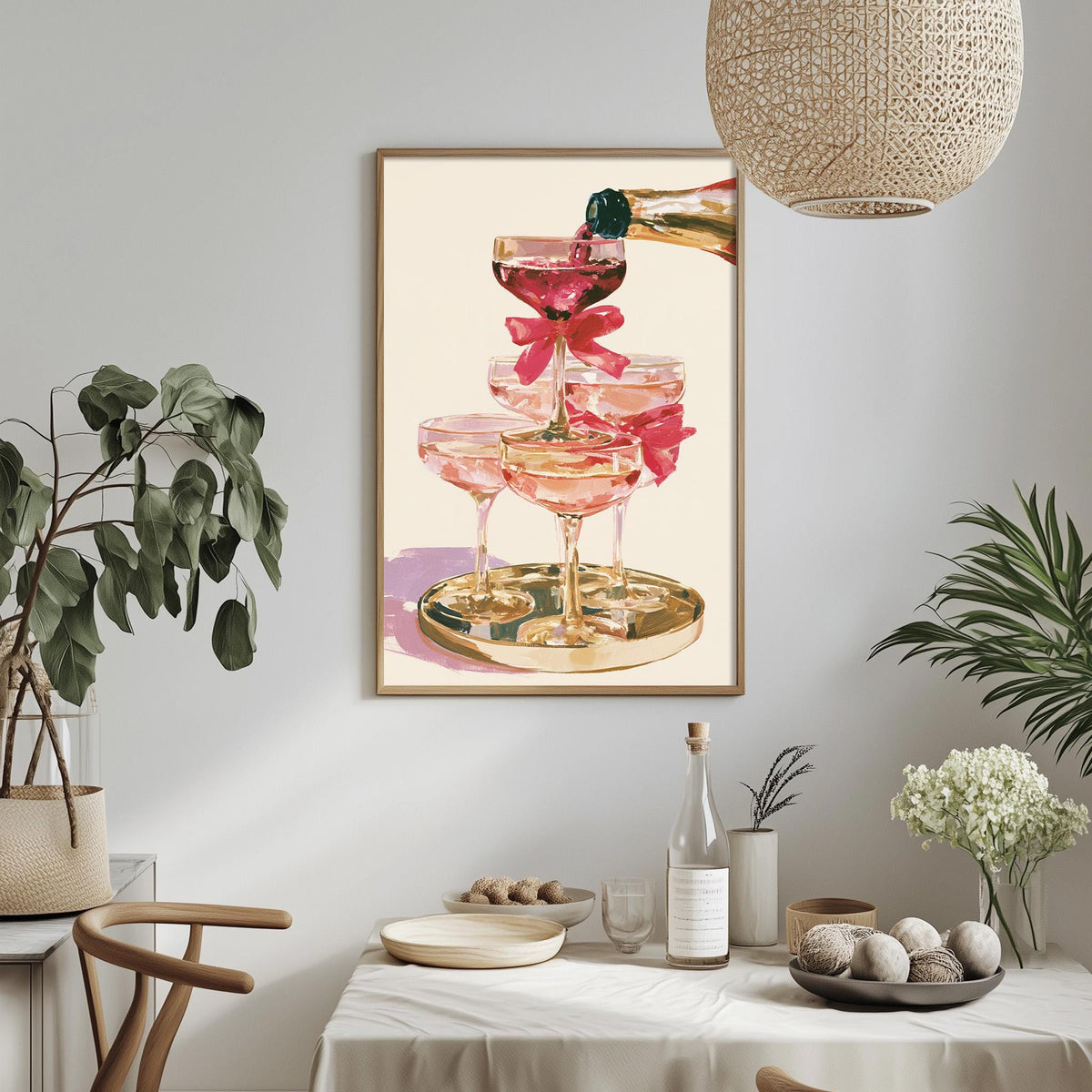 a dining table with a white tablecloth, a vase of white flowers, a bottle of wine, and a framed painting of pink champagne glasses on a gold tray.