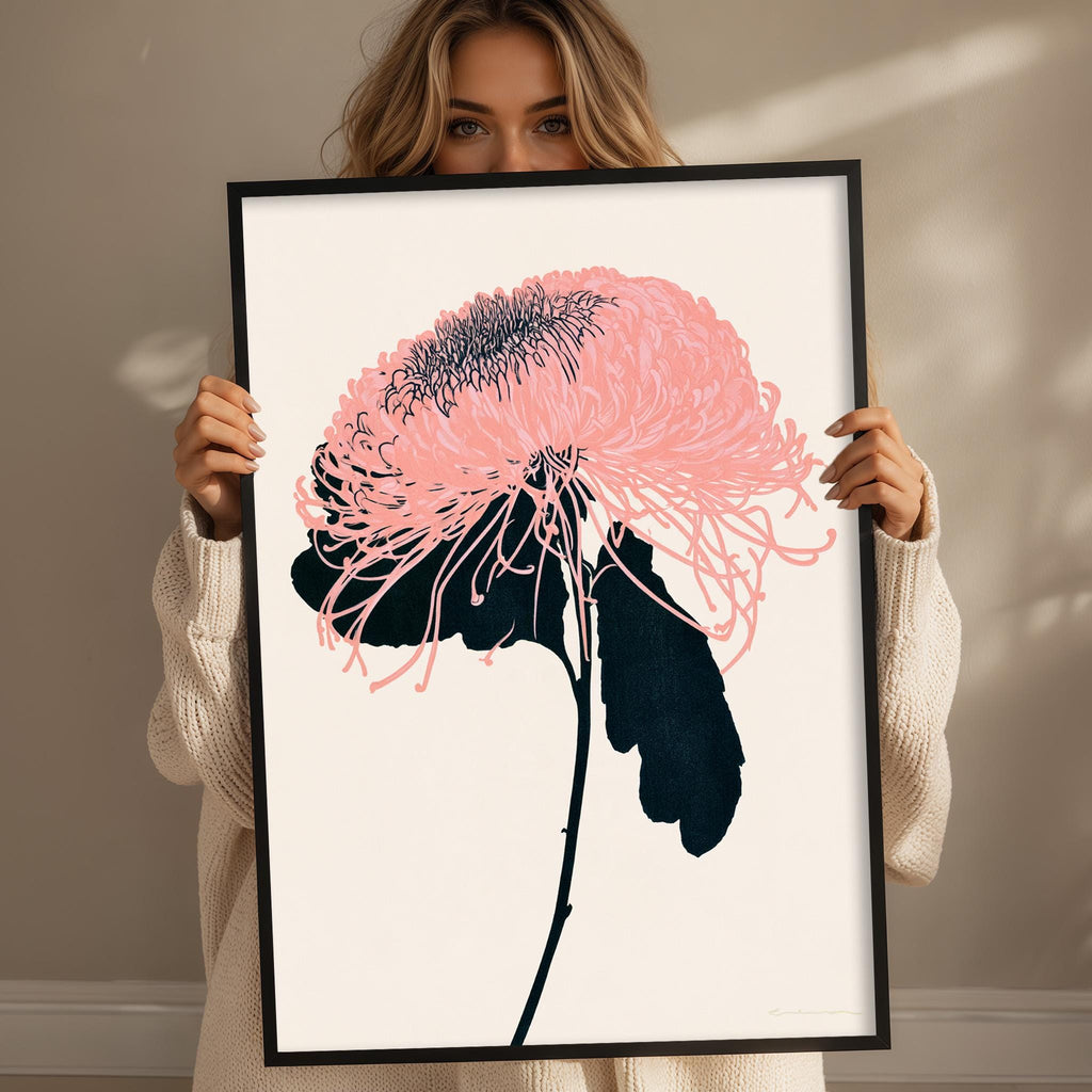 A woman holding a framed print of a pink flower with black stems and leaves.