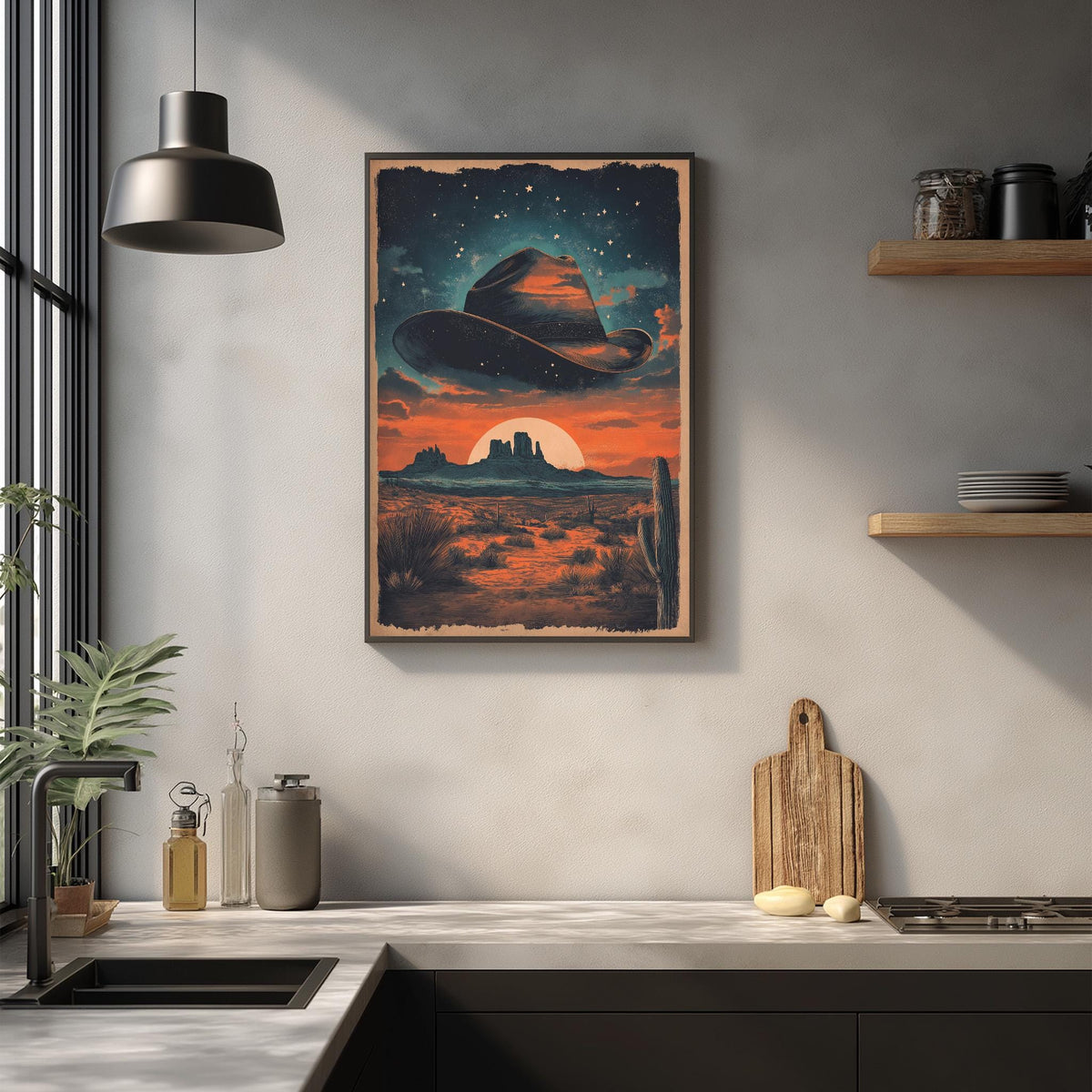 a framed artwork depicting a desert landscape with a cowboy hat in the sky, a cactus, and a sunset. The artwork is hanging on a wall above a kitchen counter with various kitchen items such as a cutting board, a bottle, and a vase.