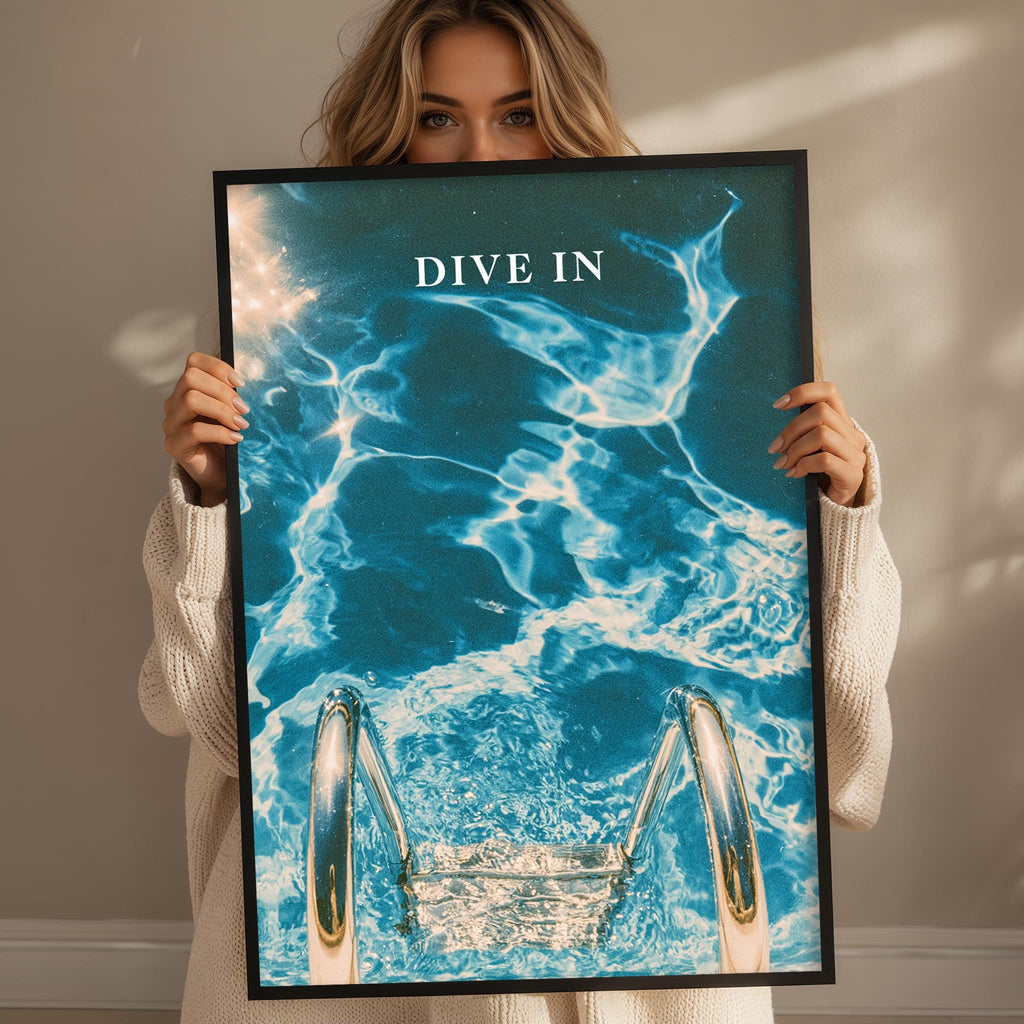 A woman holding a framed poster with a water-themed design, including a swimming pool and the text "DIVINE IN".