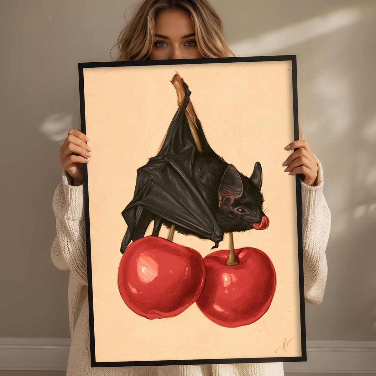 A woman holds a framed print featuring a bat perched on two red cherries.