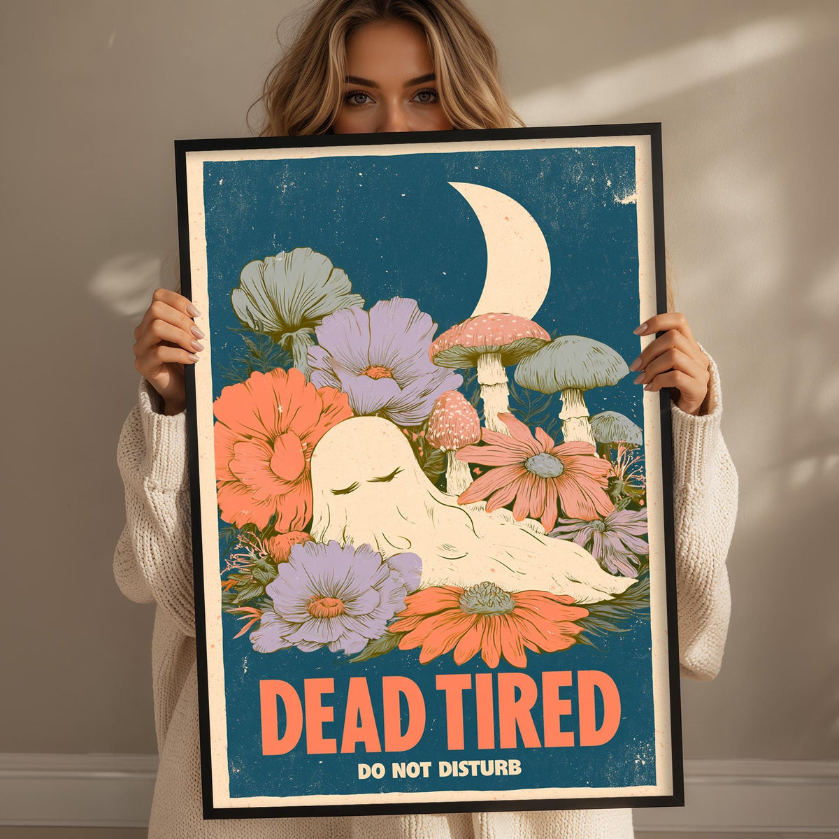 A woman holding a framed poster with a colorful illustration of flowers and mushrooms, along with the text "DEAD TIRED DO NOT DISTURB".
