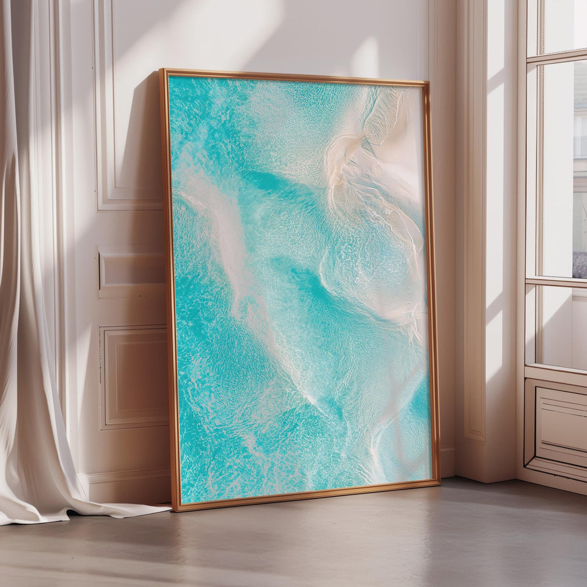 a large, framed painting of a turquoise ocean scene, with a white frame and a gold border. The painting is displayed in a corner of a room with a window, creating a serene and artistic atmosphere.
