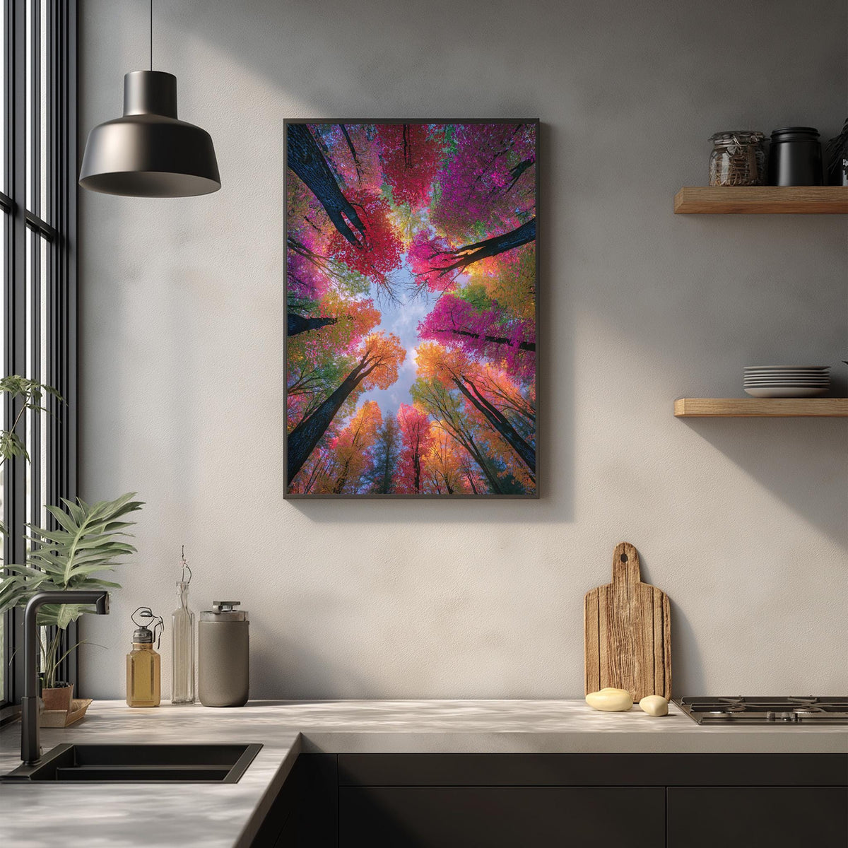 a kitchen counter with a framed picture of a forest scene hanging above it. The picture displays a vibrant and colorful view of trees with a blue sky in the background. The kitchen counter also has various items such as a cutting board, a bottle, and a vase.