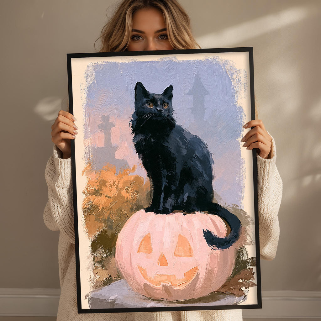 A woman holds a framed painting of a black cat sitting on a pumpkin.