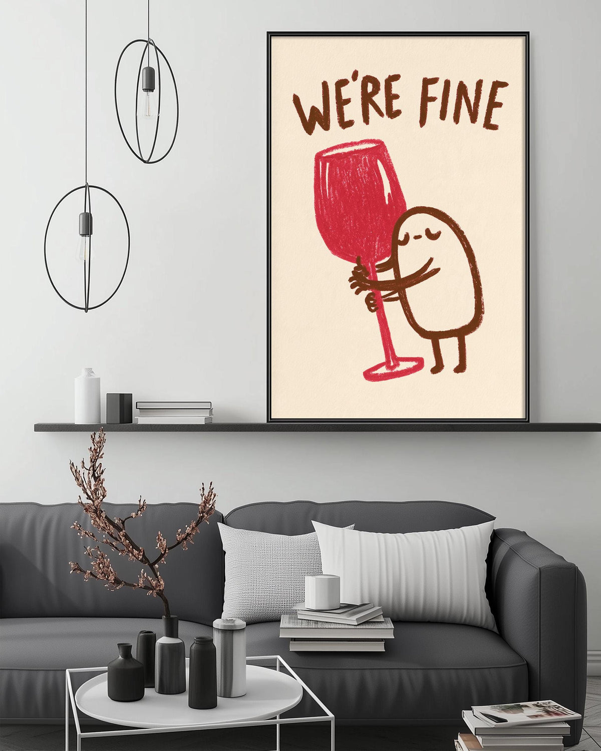 a cozy living room with a gray couch, a coffee table, and a framed poster on the wall. The poster depicts a whimsical illustration of a person holding a large red wine glass, accompanied by the text "WE'RE FINE".