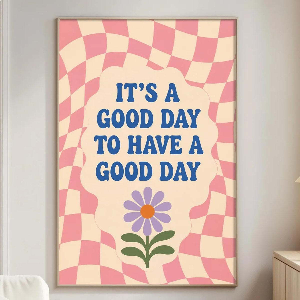 a poster with a checkered pink and white background, a purple flower, and the text "It's a good day to have a good day" written in blue.