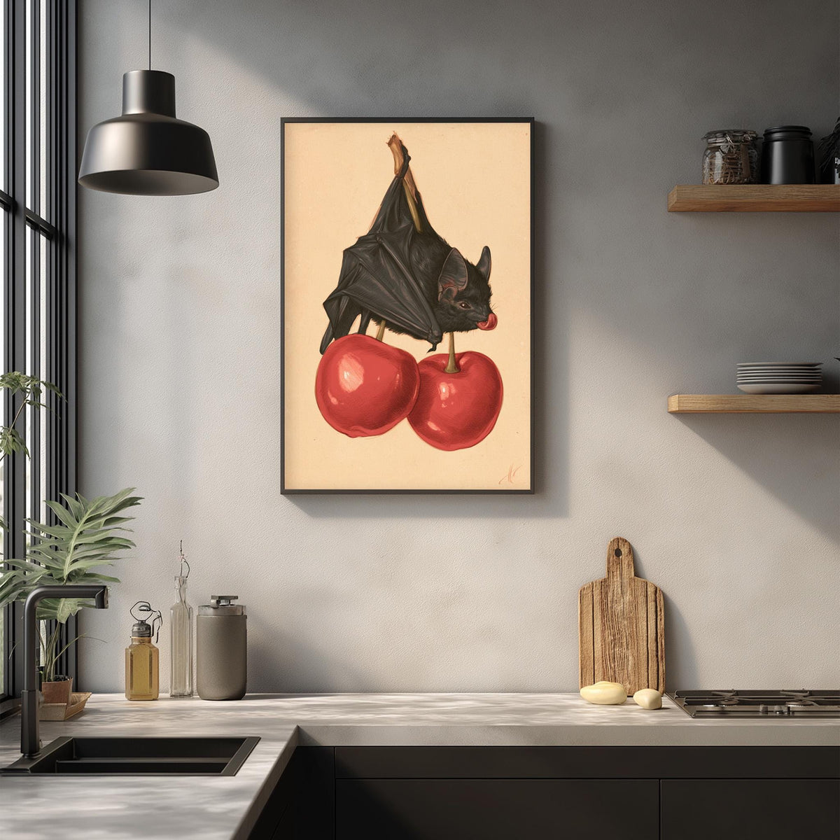 a framed artwork of a bat perched on two red cherries, hanging on a wall above a kitchen counter.