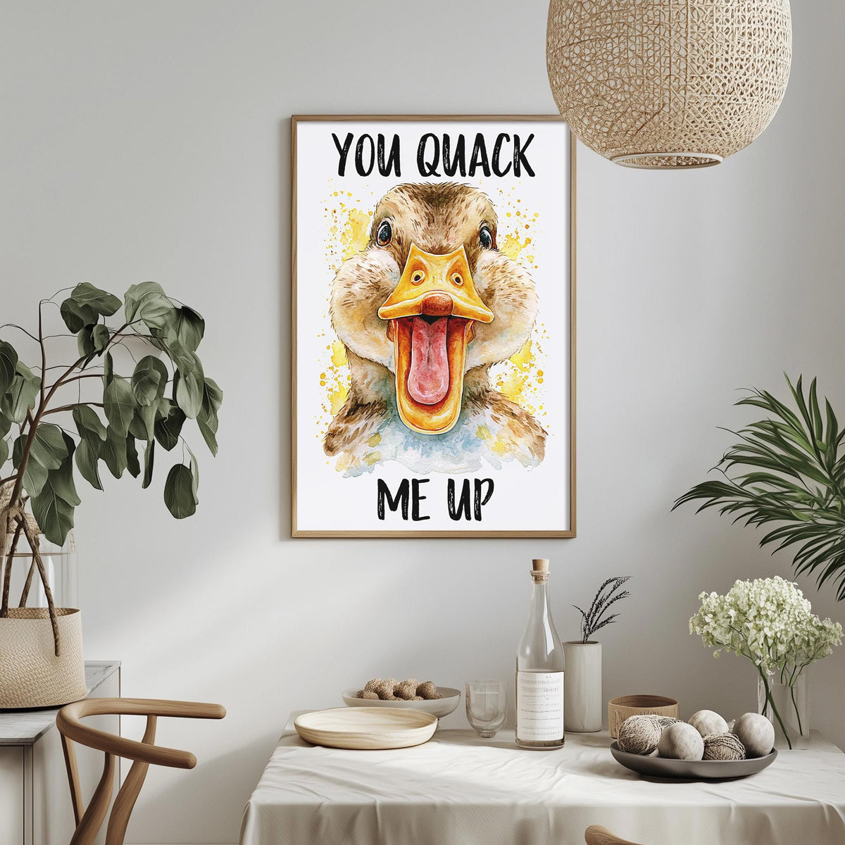 a framed poster of a duck with a humorous text that reads "YOU QUIACK ME UP", hanging on a wall above a dining table with various items on it.