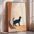 A framed illustration of a black cat standing on a wooden floor, with a person's leg visible in the background.