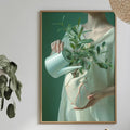 a dining table with a white tablecloth, a vase of flowers, a bottle, and a bowl of fruit. A framed painting of a woman holding a plant is hanging on the wall above the table.