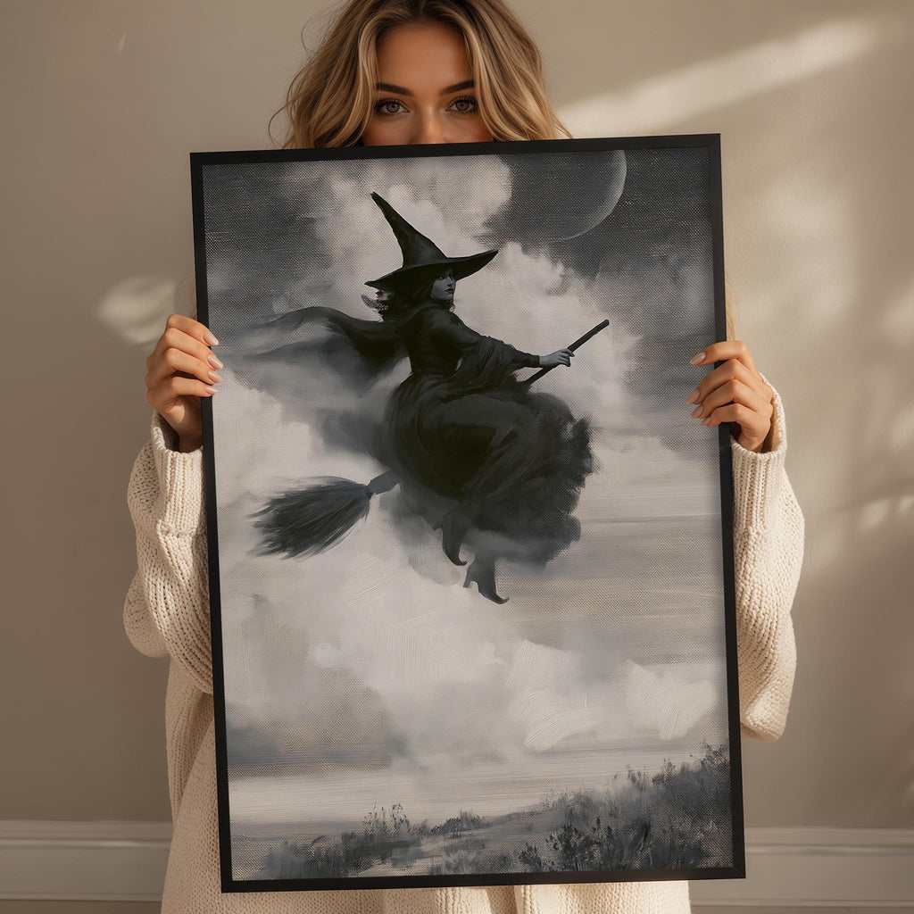 A woman holding a framed picture of a witch riding a broomstick in the sky.