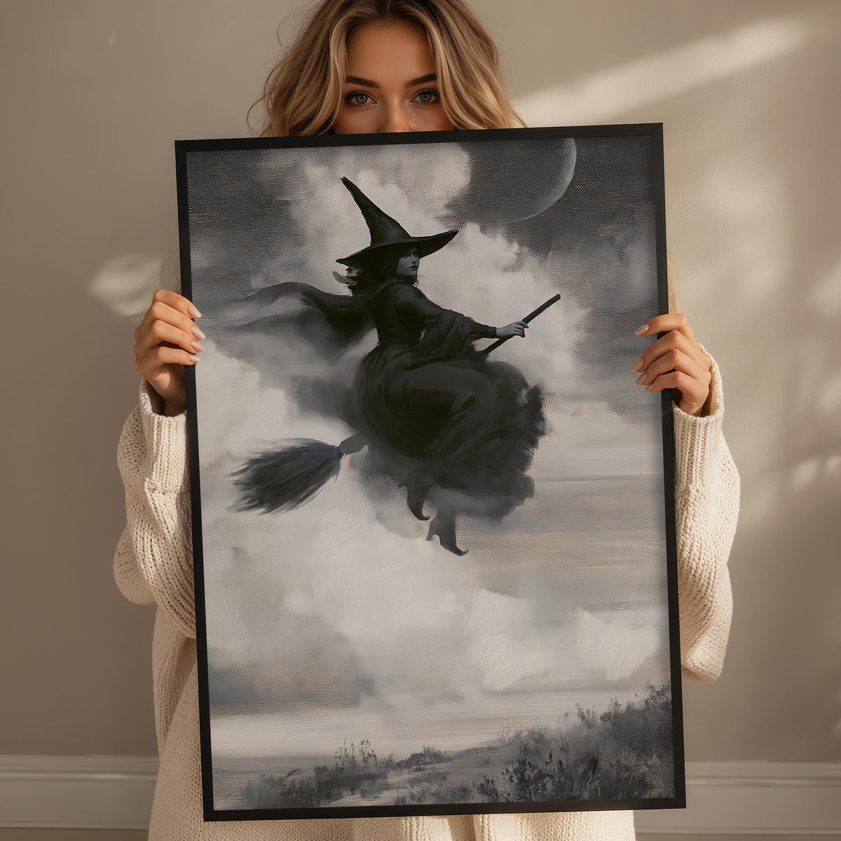 A woman holding a framed picture of a witch riding a broomstick in the sky.
