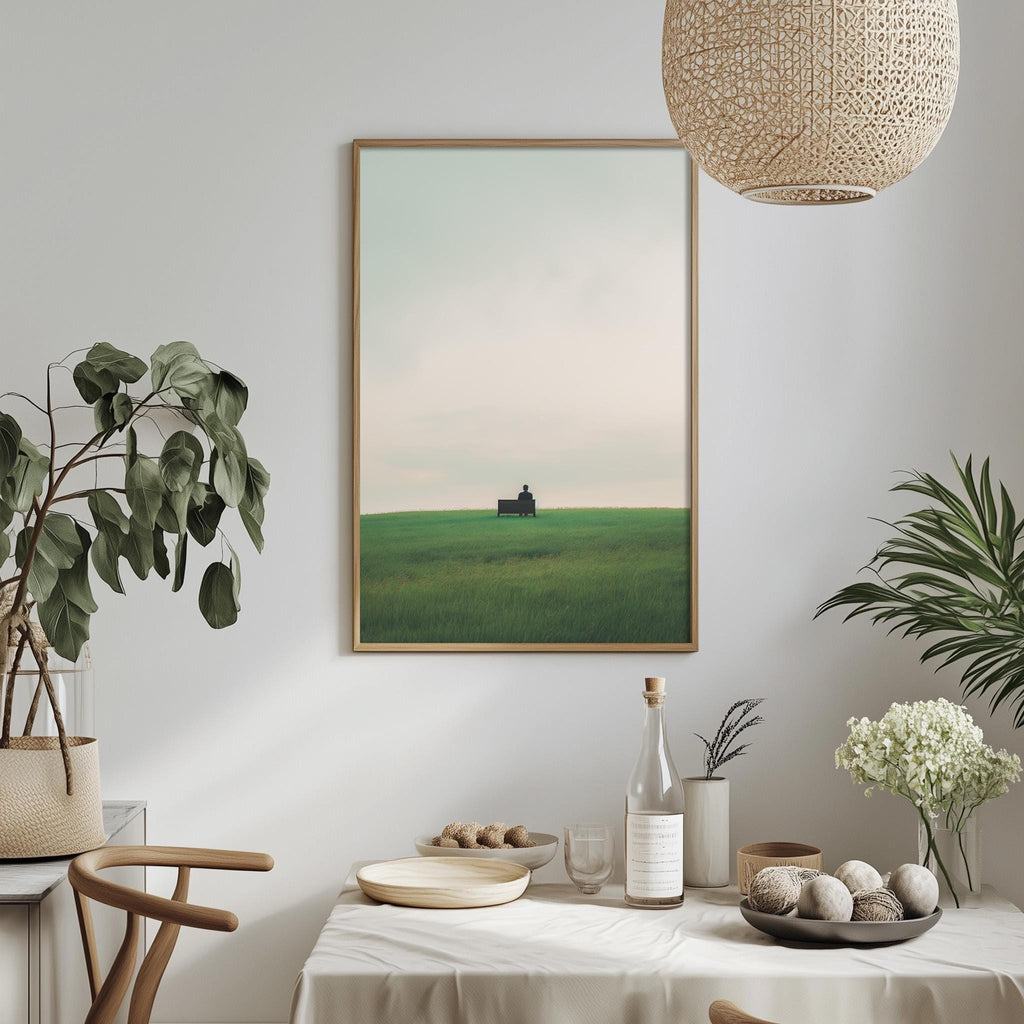 a serene dining scene with a framed picture of a green field and a small building in the distance, hanging on a white wall above a table set with plates, bowls, and a bottle of wine.