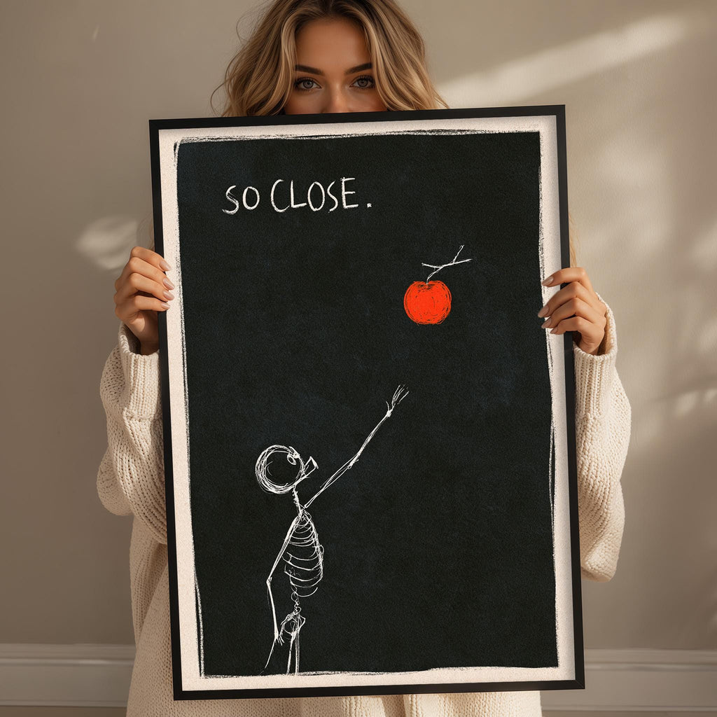 A woman is holding up a framed artwork that depicts a skeleton reaching for an apple against a black background.