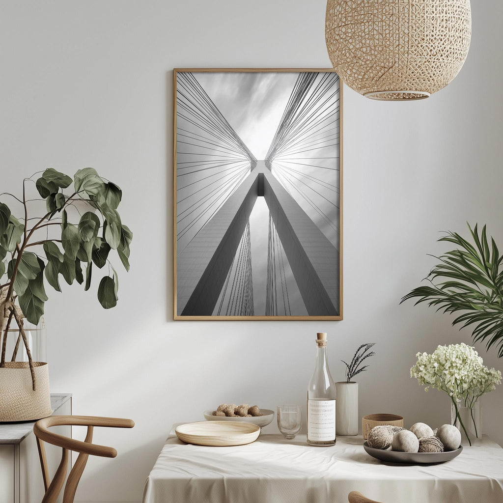 a dining table set with a white tablecloth, a bowl of fruit, a bottle, and a vase with flowers. A framed photograph of a building with a unique design hangs on the wall above the table.