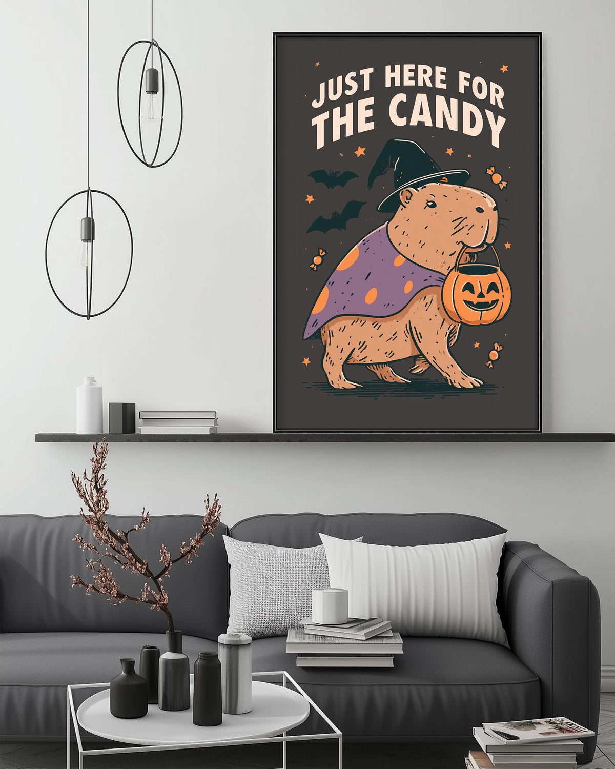 a cozy living room with a gray couch, a coffee table, and a large framed poster of a cartoon character holding a pumpkin and wearing a witch's hat. The poster has the text "Just here for the candy" written on it.