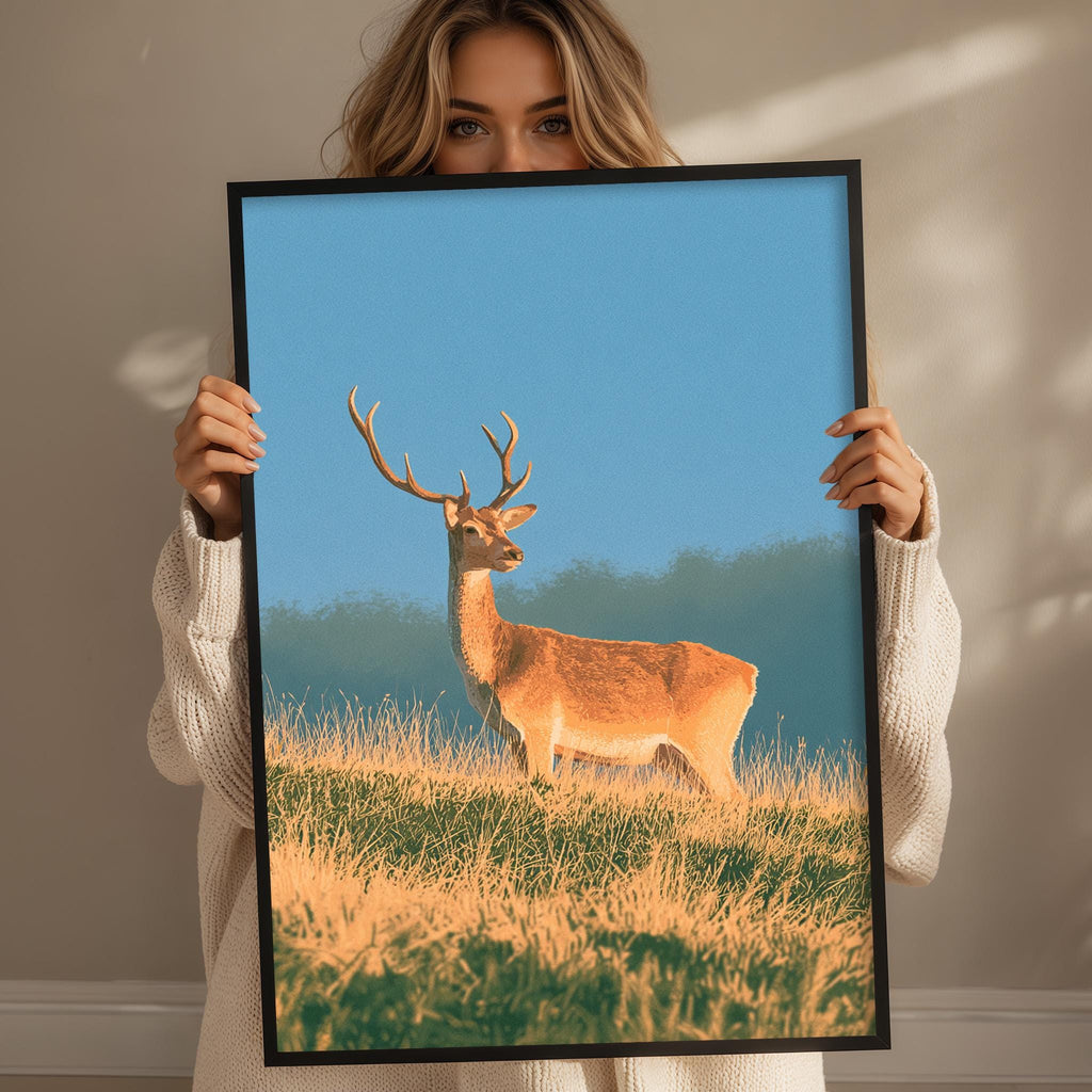A woman holds up a framed picture of a deer standing in a grassy field against a blue sky.