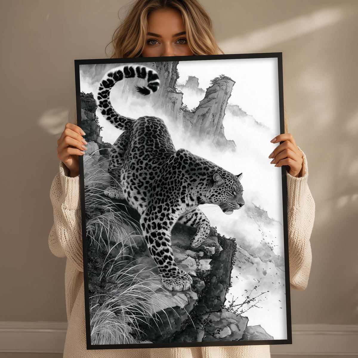 A woman holds up a framed black and white image depicting a leopard on a rocky cliff.