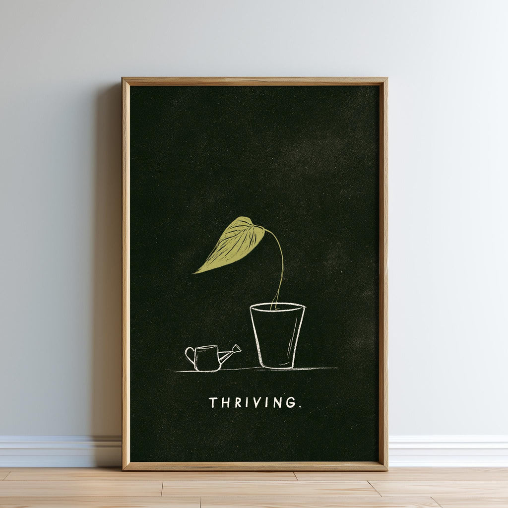 The image is a framed poster with a black background and a white illustration of a plant with a yellow leaf. The plant is in a small pot, and there is a watering can next to it. The word "THRIVING" is written below the illustration.