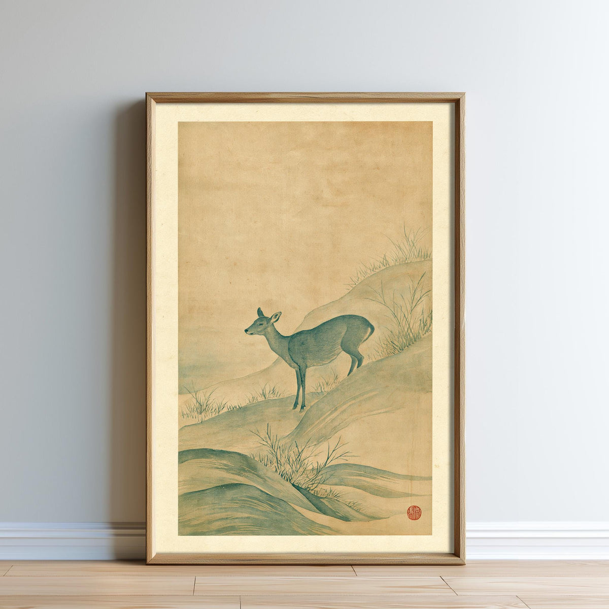 The image is a framed painting depicting a deer standing on a hillside with grass and rocks.