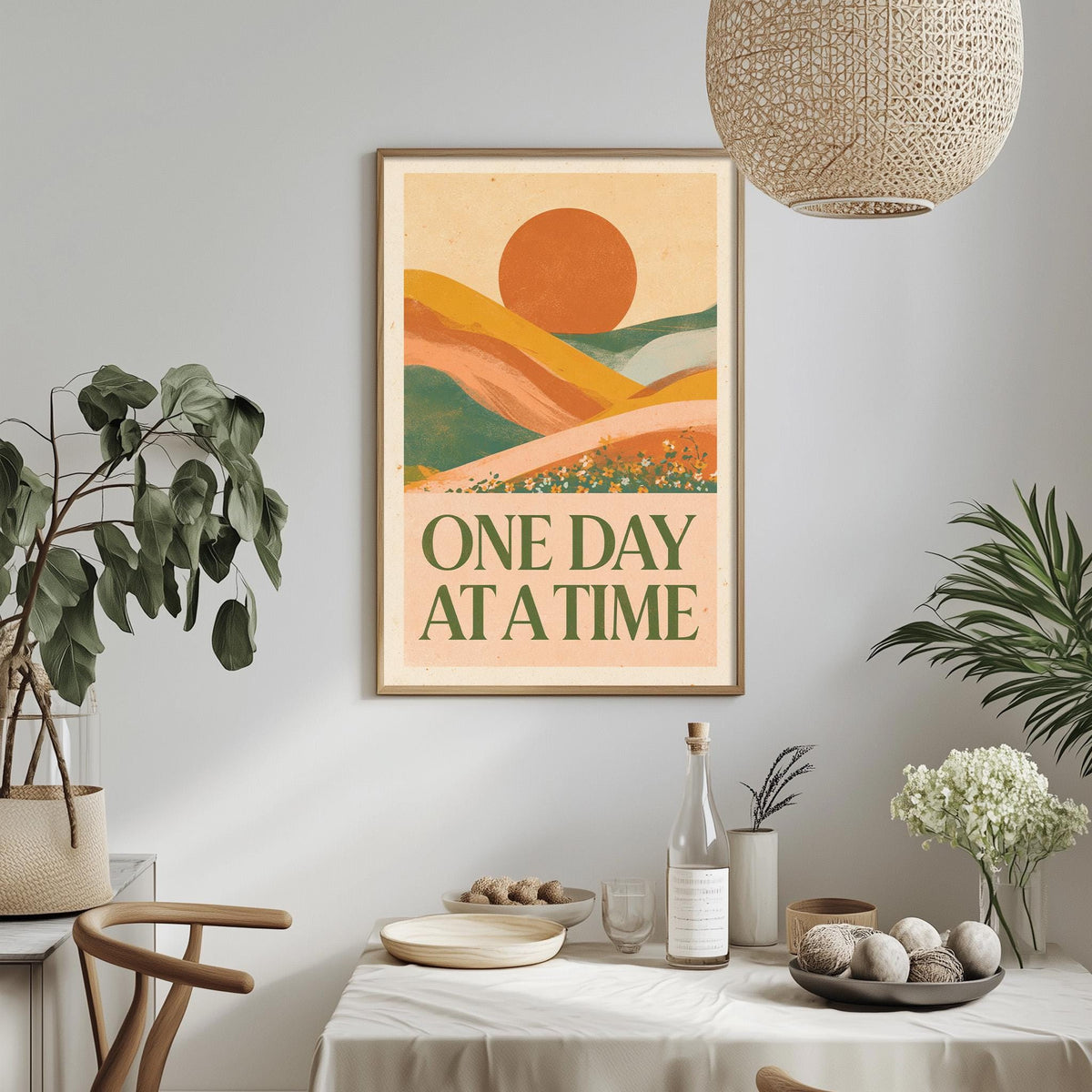 a framed poster with a landscape scene and the text "ONE DAY AT A TIME" hanging on a wall above a dining table with various items on it.