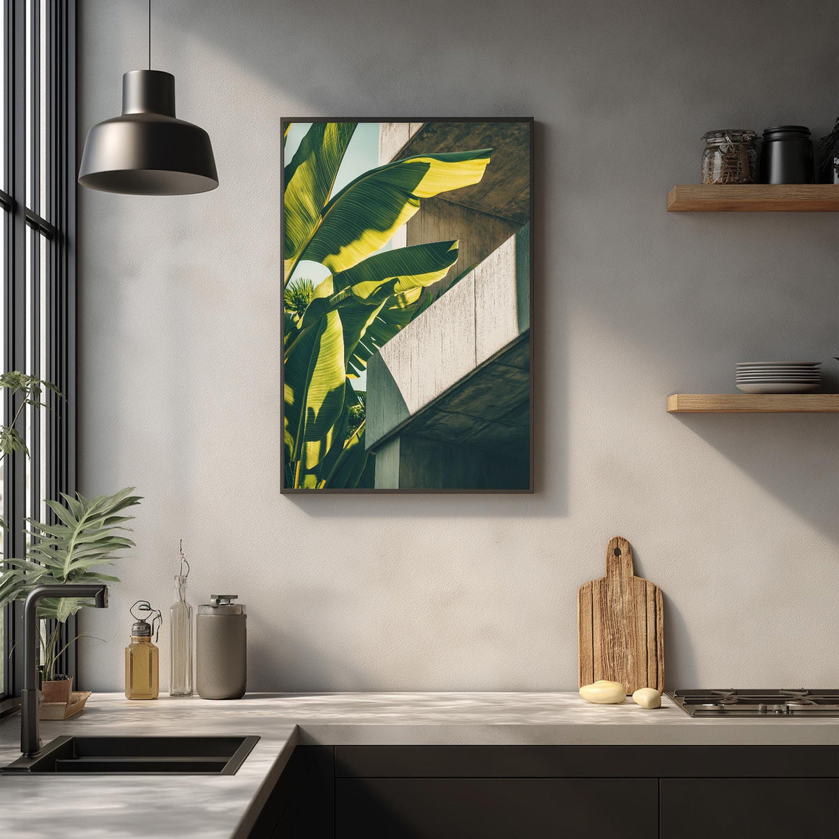 a kitchen counter with various items on it, including a wooden cutting board, a bottle, and a vase. Above the counter, there is a framed picture of a banana tree hanging on the wall.