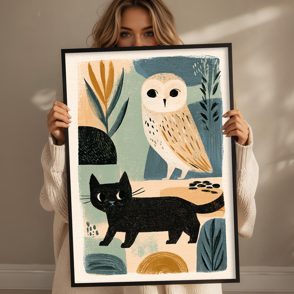 A woman is holding up a framed artwork featuring an illustration of a black cat and an owl.