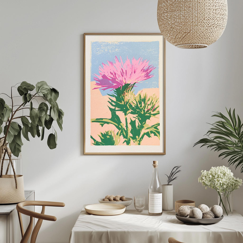 a dining table with a white tablecloth, a bowl of fruit, a bottle, and a vase with flowers. Above the table, there is a framed print of a pink flower on a green background.