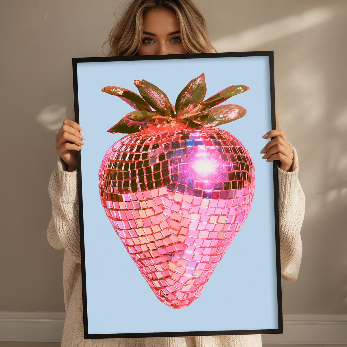 A woman holds up a framed image of a pink disco ball with a strawberry design.