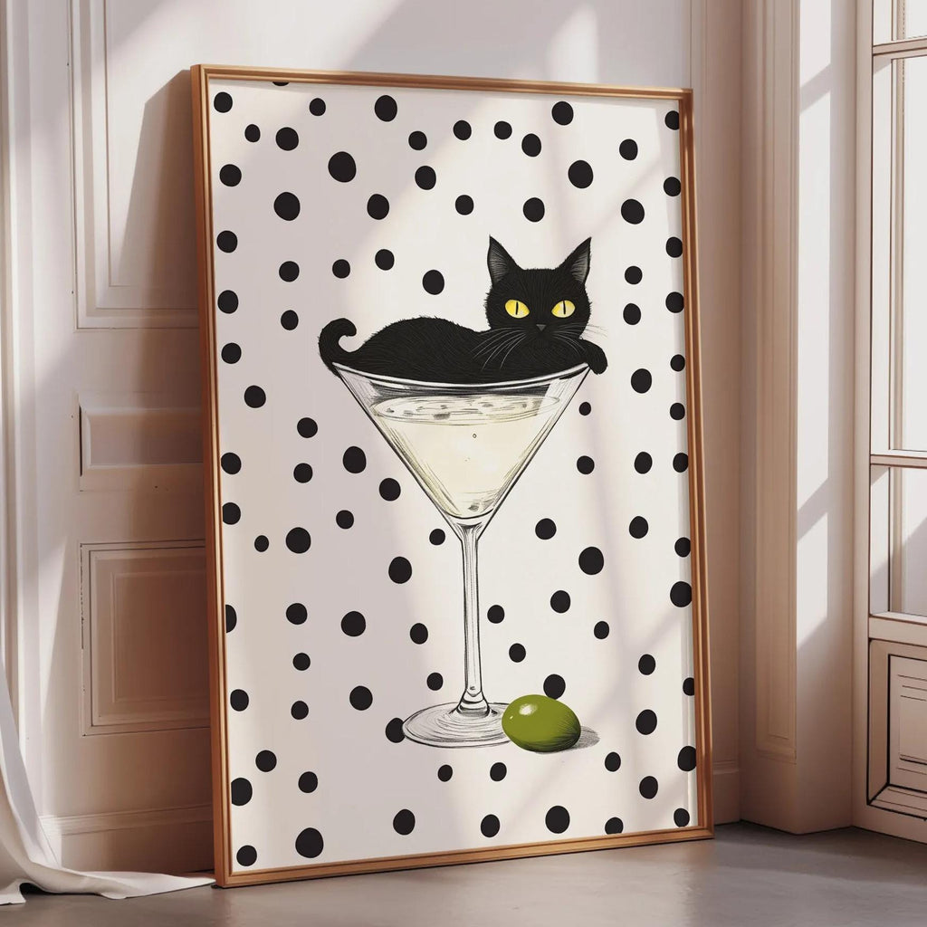 A framed poster featuring a black cat sitting on a martini glass with an olive on the rim.