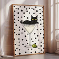 A framed poster featuring a black cat sitting on a martini glass with an olive on the rim.