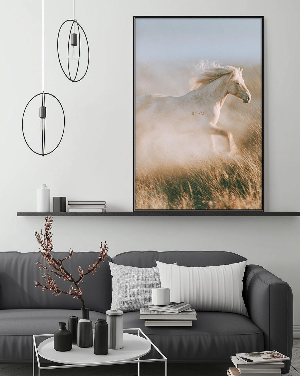 a large framed picture of a white horse running in a field, hanging on a wall above a gray couch with white pillows.