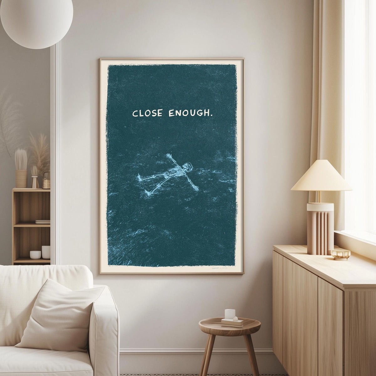 a living room with a white couch, a wooden side table, and a framed poster on the wall. The poster has a blue background with a white text that says "CLOSE ENOUGH."