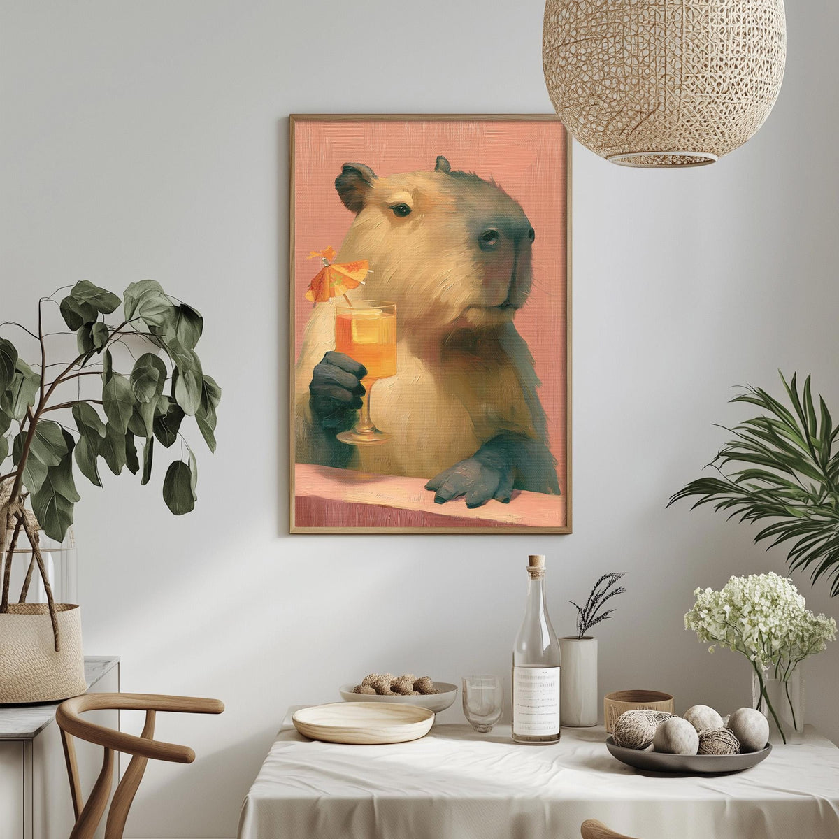 a painting of a capybara holding a glass of orange juice, hanging on a wall above a table with various items on it.