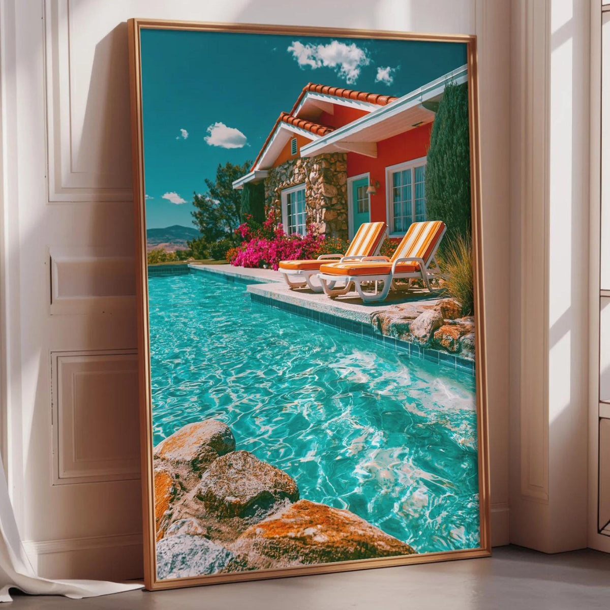 A large framed picture depicting a colorful tropical house with a swimming pool and lounge chairs, set against a bright blue sky with fluffy clouds.