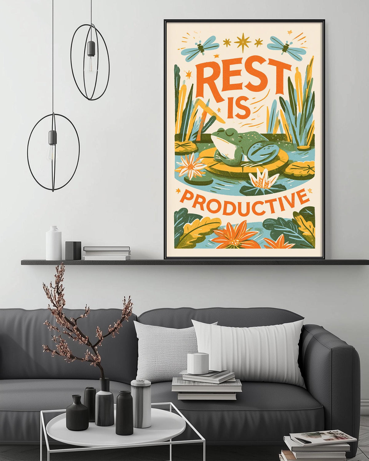a living room with a gray couch, a coffee table, and a framed poster on the wall. The poster has a colorful illustration of a frog and plants, along with the text "REST IS PRODUCTIVE".