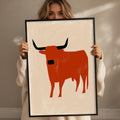 A woman holding a framed picture of a red bull.