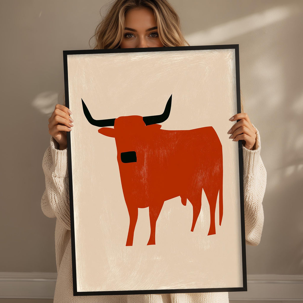 A woman holding a framed picture of a red bull.