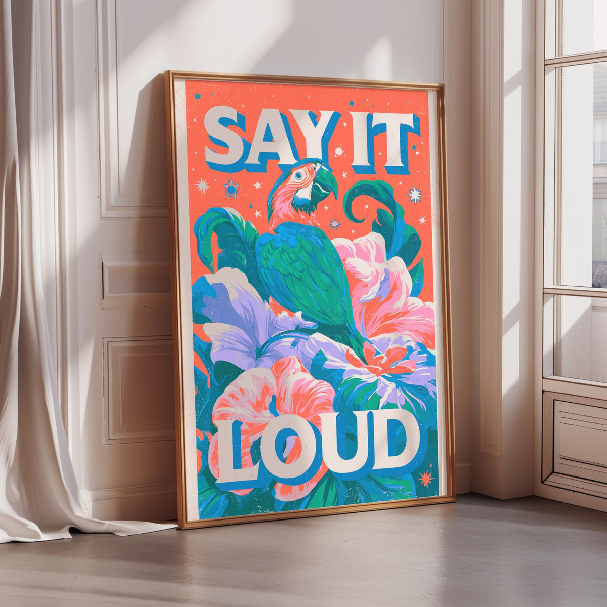 A framed poster with a vibrant illustration of a parrot surrounded by colorful flowers and leaves, with the text "SAY IT LOUD" prominently displayed.