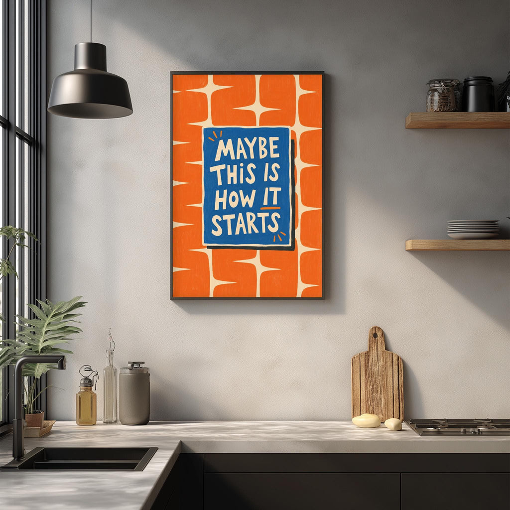 a kitchen counter with a framed poster hanging on the wall above it. The poster has a bold, colorful design with the text "MAYBE THIS IS HOW IT STARTS" written in white letters. The kitchen counter has various items on it, including a cutting board, a bottle, and a plant.