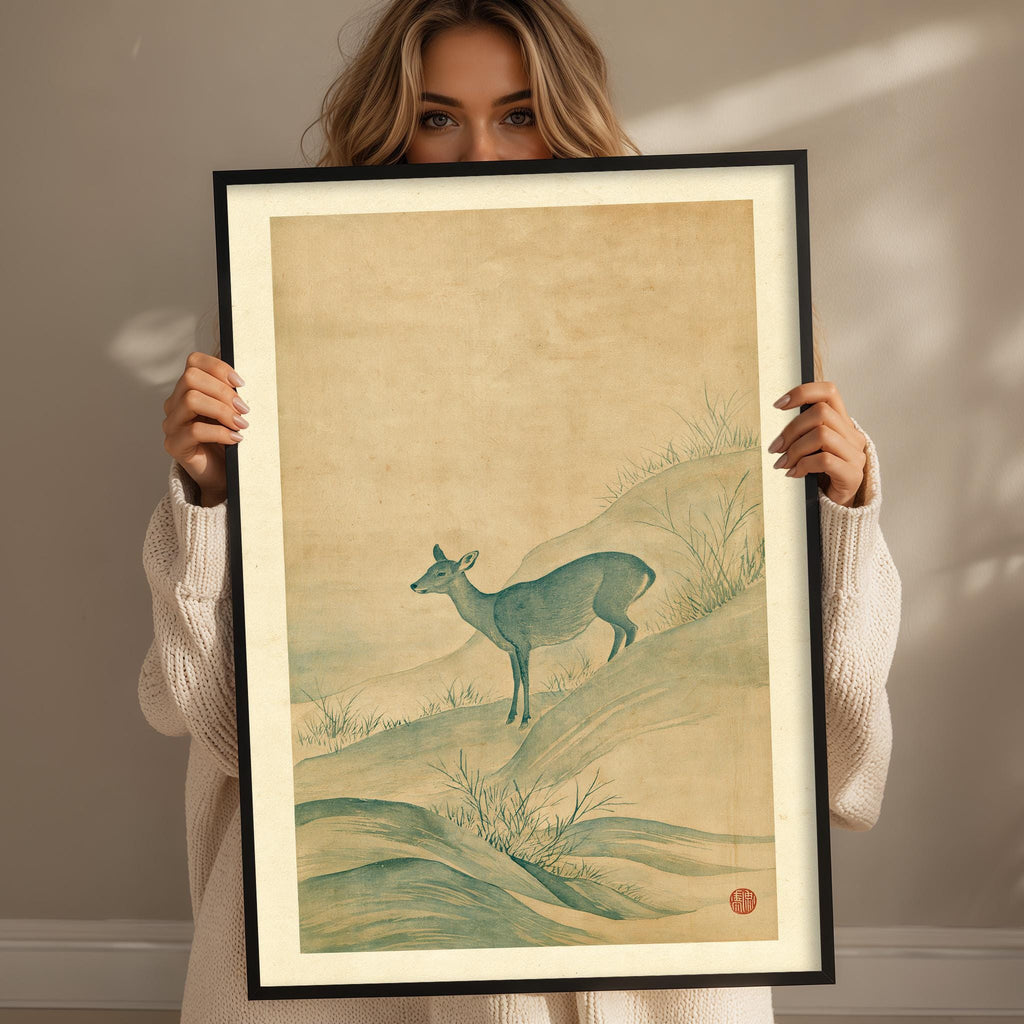 A woman holds a framed picture of a deer standing on a hill, with a serene landscape in the background.