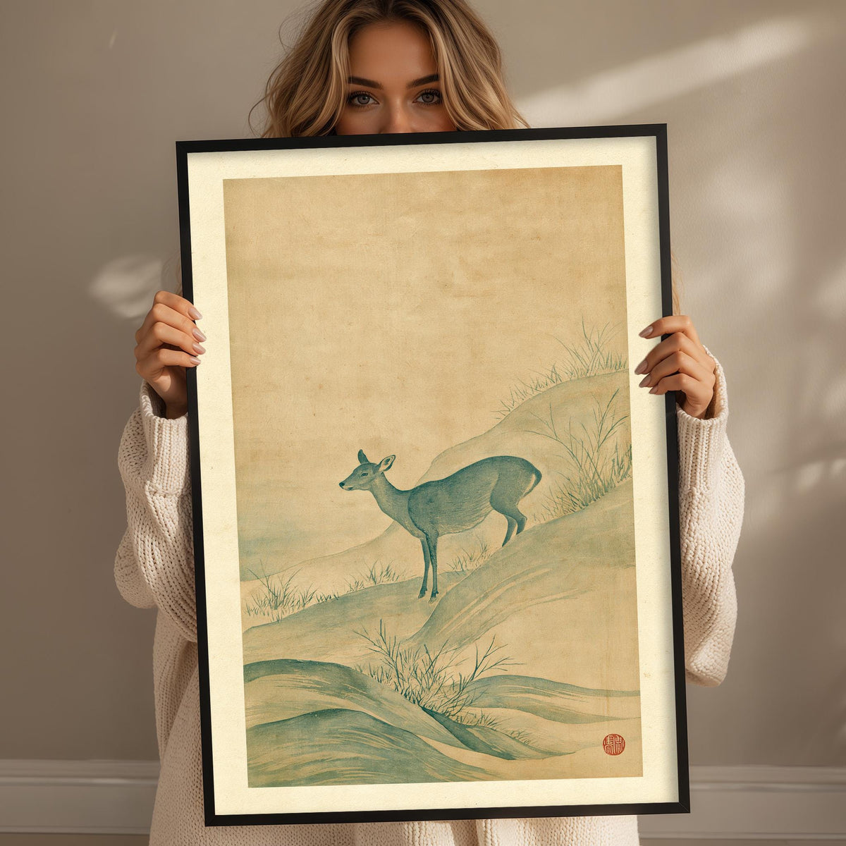 A woman holds a framed picture of a deer standing on a hill, with a serene landscape in the background.