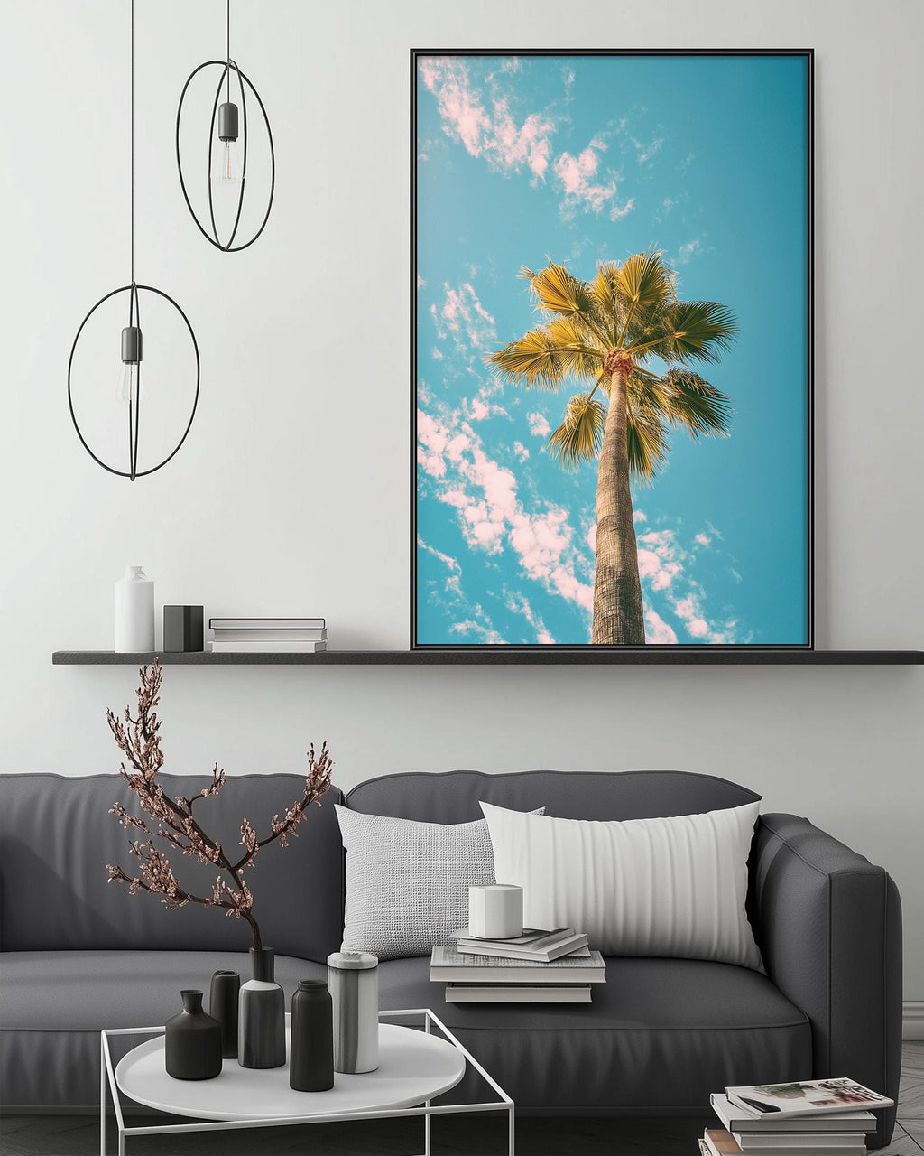 a large framed picture of a palm tree against a blue sky with clouds, hanging on a wall above a gray couch with white pillows.
