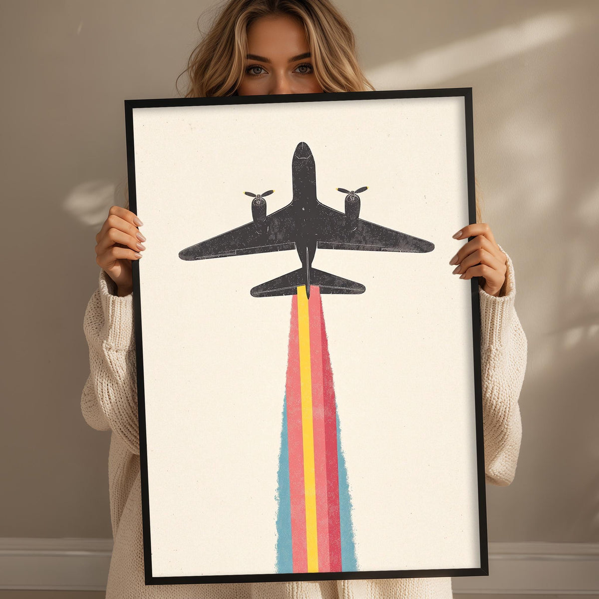 A woman holding a framed picture of a plane with a rainbow-colored smoke trail.