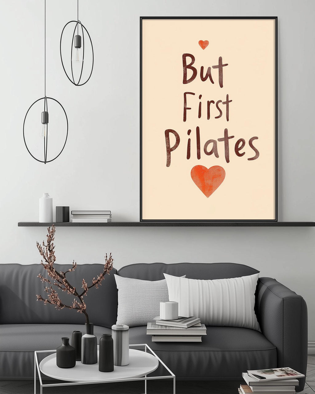 a living room with a gray couch, a coffee table, and a framed poster with the text "But First Pilates" and an orange heart.