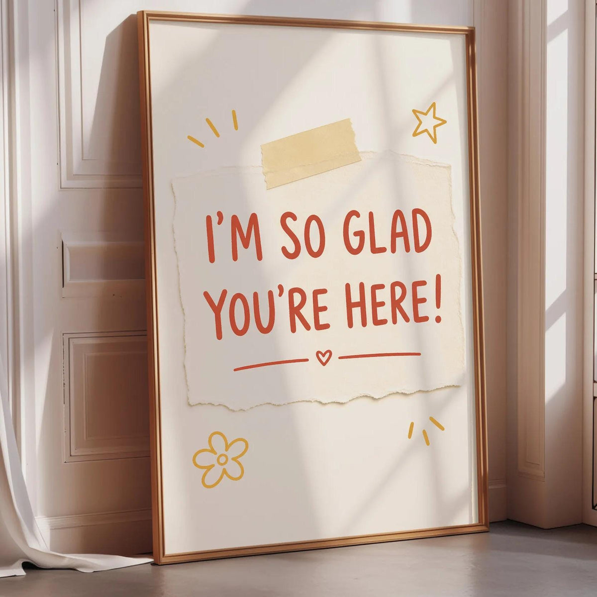 A framed poster with the text "I'm so Glad You're Here!" displayed on it, along with some decorative elements such as a flower and a star.
