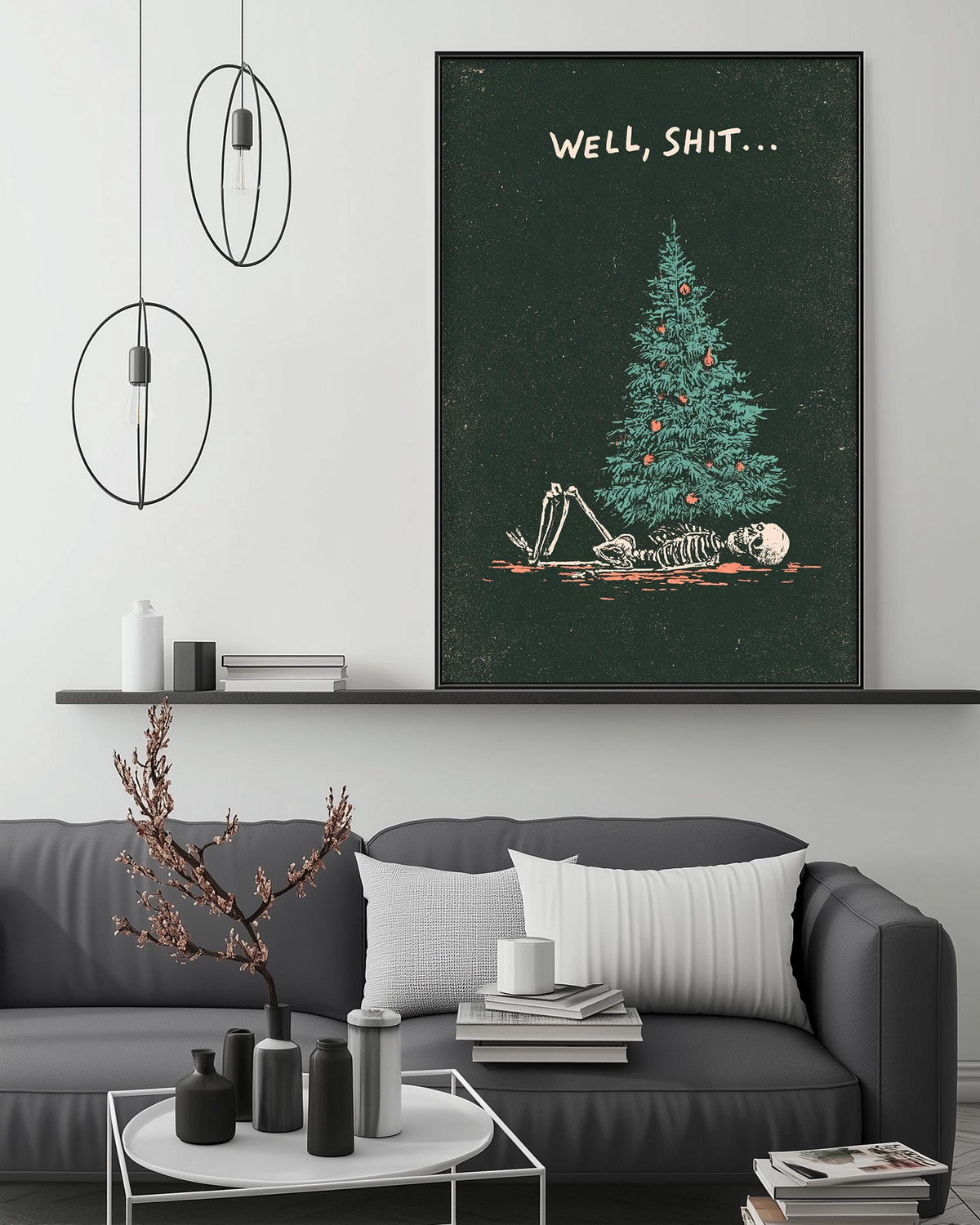 a living room with a gray sofa, a coffee table, and a large framed poster of a skeleton lying on a Christmas tree. The poster has the text "WELL, SHIT..." written on it.